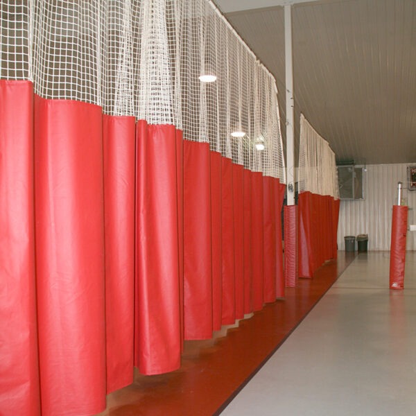 Row of red punching bags lining a training facility with white netting above and a gray floor.
