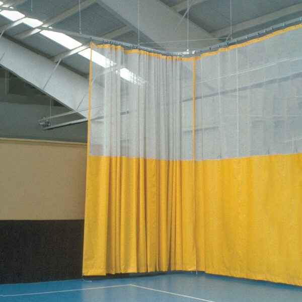 Tall yellow and clear curtain divider in a gym, separating sections of the blue-floored space under an industrial ceiling.