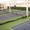 23955Z-3 | National Sports Products Indoor tennis facility with multiple blue courts and green surrounding walls; two players stand at the net on a central court as others play in the background