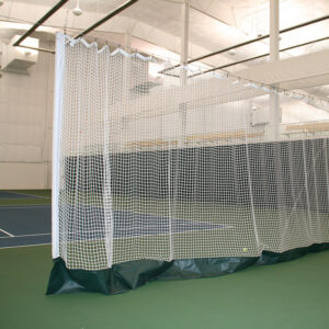 Indoor gym with a white mesh netting enclosure forming a practice cage on green flooring and padded base.