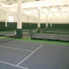 23955Z-6 | National Sports Products Indoor tennis facility with multiple courts, nets, and white support pillars with green divider curtains in the background.