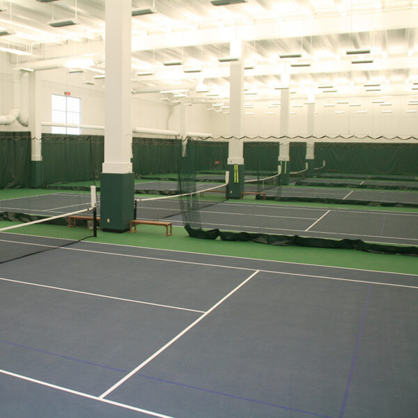 23955Z-6 | National Sports Products Indoor tennis facility with multiple courts, nets, and white support pillars with green divider curtains in the background.